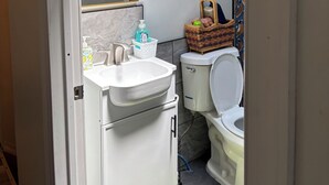 Une salle de bain avec un lavabo blanc, un miroir, des toilettes et un panier contenant des articles de toilette.