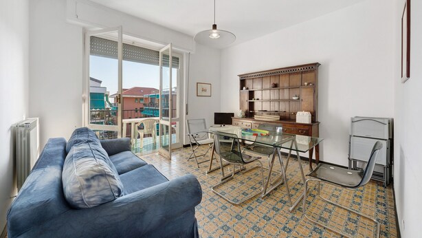 Un salon comprenant un canapé, une table en verre, un fauteuil, un coin cuisine avec des placards et une vue à travers une porte vitrée.