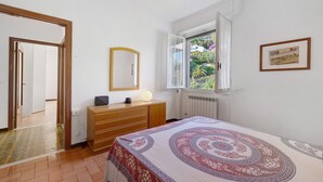 Une chambre à coucher comprenant un lit, une commode, un miroir, une fenêtre avec vue et une porte donnant sur une autre pièce.