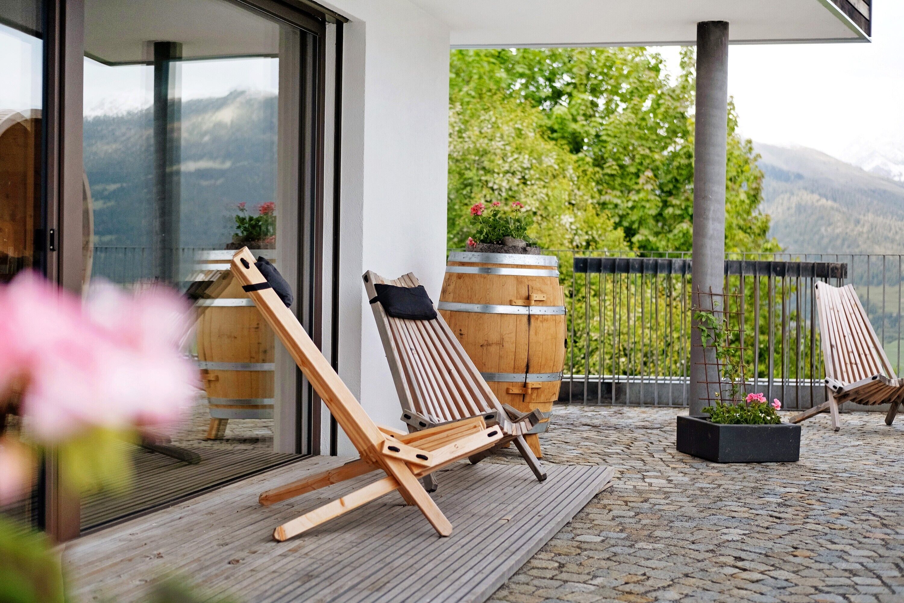 A wooden deck with two lounge chairs, a potted plant, and a view of mountains.