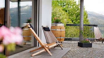 A wooden deck with two lounge chairs, a potted plant, and a view of mountains.