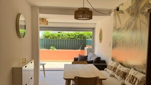 A modern living room with a dining area, a sofa with 'HAPPY FAMILY' pillows, a large mirror, and a view of greenery outside. - T2bis - Cap d'Agde - 40 m² with terrace, swimming pool, parking & 200 m from the beach (Agde)