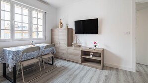 A room with a dining table, chairs, a TV, a cabinet, and a window.