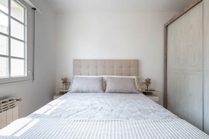 Un dormitorio con cama, dos mesitas de noche, una ventana y un armario.