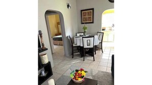 A dining area with a table set for four, a vase with flowers, and a remote control on the table.
