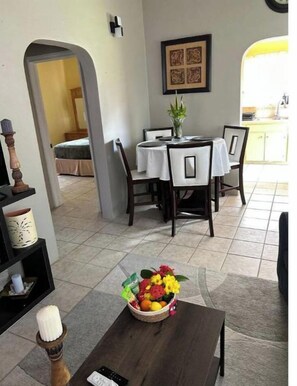 A dining area with a table set for four, a vase with flowers, and a remote control on the table.