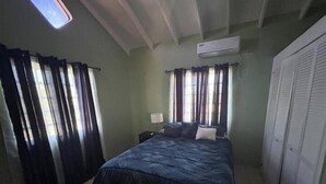 A bedroom with a bed, curtains, a nightstand, a lamp, an air conditioner, and a wardrobe.
