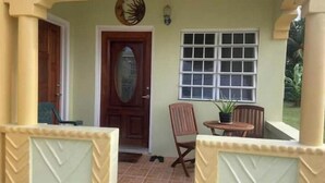 A covered porch with a wooden door, a window with multiple panes, and a small table with a potted plant.