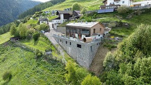 Ein Anwesen an einem Hang mit einer Mauer aus Stein, einem Holzhaus und einem modernen Gebäude mit Balkonen.