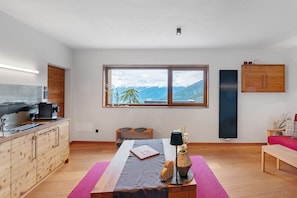 A modern room with a kitchen, a dining area, and a large window with a mountain view.