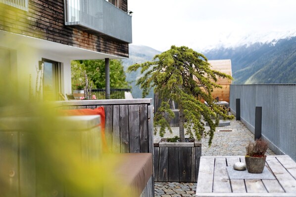 A wooden deck with a potted plant, a bench, and a view of mountains.