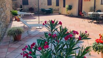 A courtyard with a tiled floor, potted plants, outdoor furniture, and a building with a tiled roof.
