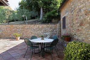 Un muro de piedra, una mesa redonda con sillas y plantas en macetas.