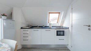 Una cocina compacta con armarios blancos, horno empotrado, ventana y un refrigerador pequeño.