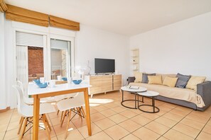 A modern living room with a dining table, sofa, TV, and a small side table.