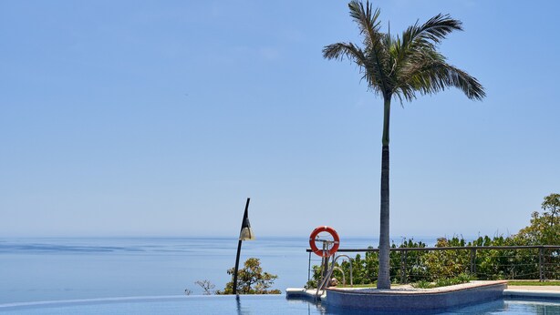 Cielo azul despejado, una piscina, un flotador, una palmera y una bandera.