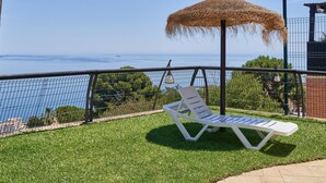 Un balcón con una silla lounge blanca, un toldo de paja y vistas al mar.