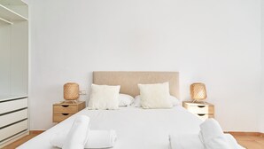 Una cama bien hecha con sábanas y almohadas blancas, dos mesitas de noche con lámparas y un cabecero de madera.