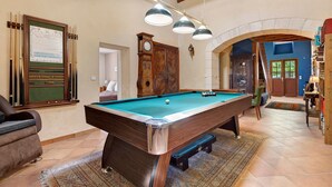 A pool table with a clock, a wooden cabinet, and a staircase leading to a second floor.