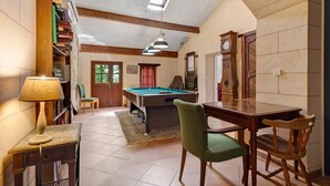 A room with a pool table, bookshelves, a lamp, a chair, and a clock.