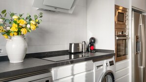 A modern kitchen with a built-in oven, a washing machine, and a coffee maker on the counter. - Apartment 'Reyes Católicos Conil' with Wi-Fi and Air Conditioning (Conil de la Frontera)