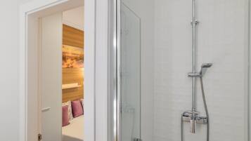 Een moderne badkamer met een douchecabine van glas, een handdouche en een wandmengkraan.