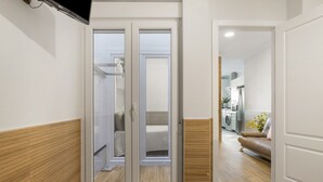 A modern interior with a sliding door leading to a bathroom, a sofa in a living area, and a kitchen visible through an open door. - Apartment 'Reyes Católicos Conil' with Wi-Fi and Air Conditioning (Conil de la Frontera)