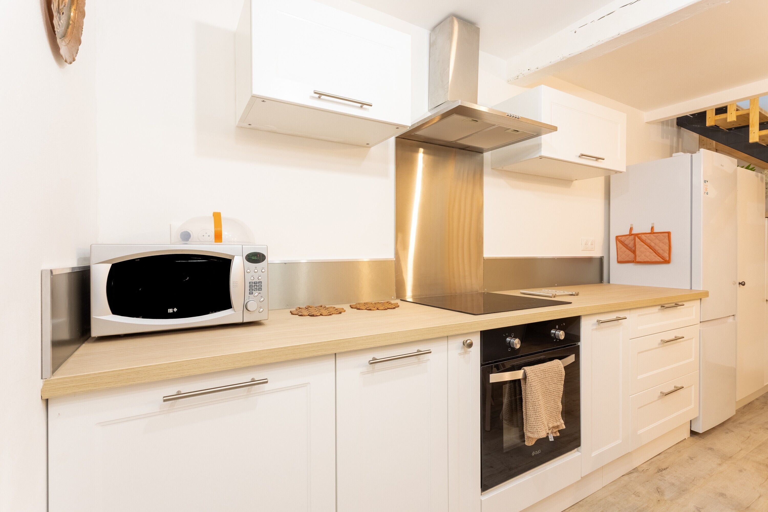 A modern kitchen with white cabinets, a stainless steel range hood, a microwave, an oven, and a refrigerator.