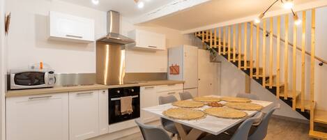 Une cuisine moderne avec des armoires blanches, une hotte en acier inoxydable et un coin repas avec une table dressée pour quatre personnes.