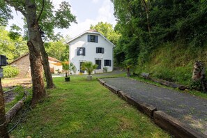 Una casa a due piani con vialetto lastricato, immersa nel verde e circondata da alberi.