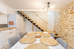 Una cocina moderna con armarios blancos, una escalera de madera y una pared de piedra.