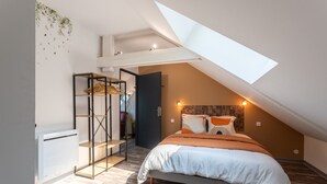 A bedroom with a sloped ceiling, a bed with white and orange bedding, a wooden floor, and a skylight.