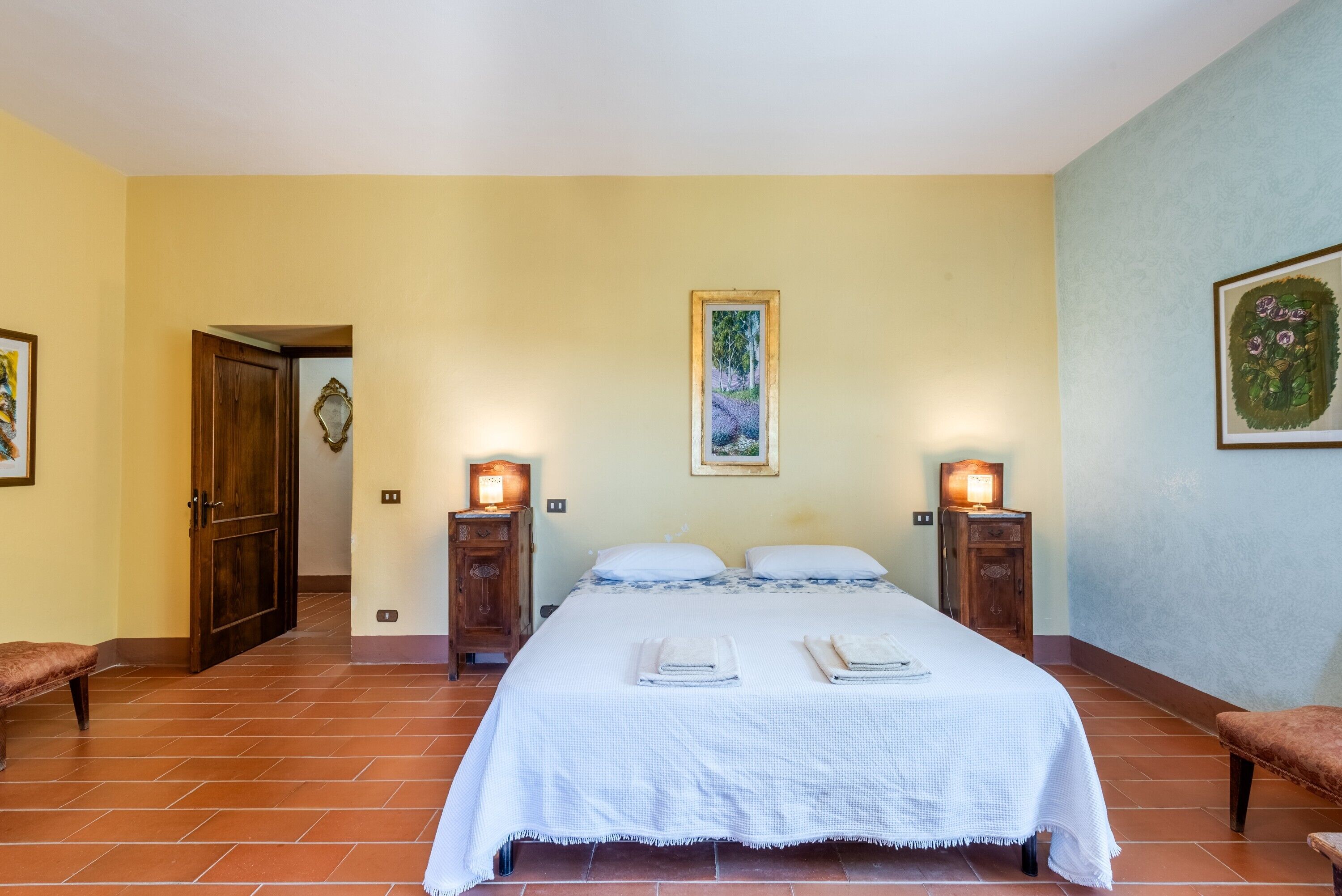 A bedroom with a bed, two bedside tables, a bench, and a door.