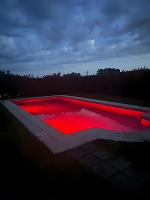Une piscine rectangulaire dont le bord est illuminé de lumières rouges, entourée d’une terrasse dallée.