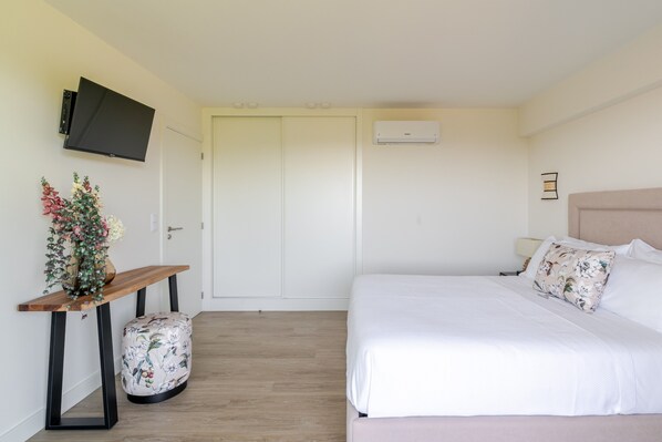 A bedroom with a bed, a TV mounted on the wall, a bedside table with a vase, and a door with a closet.