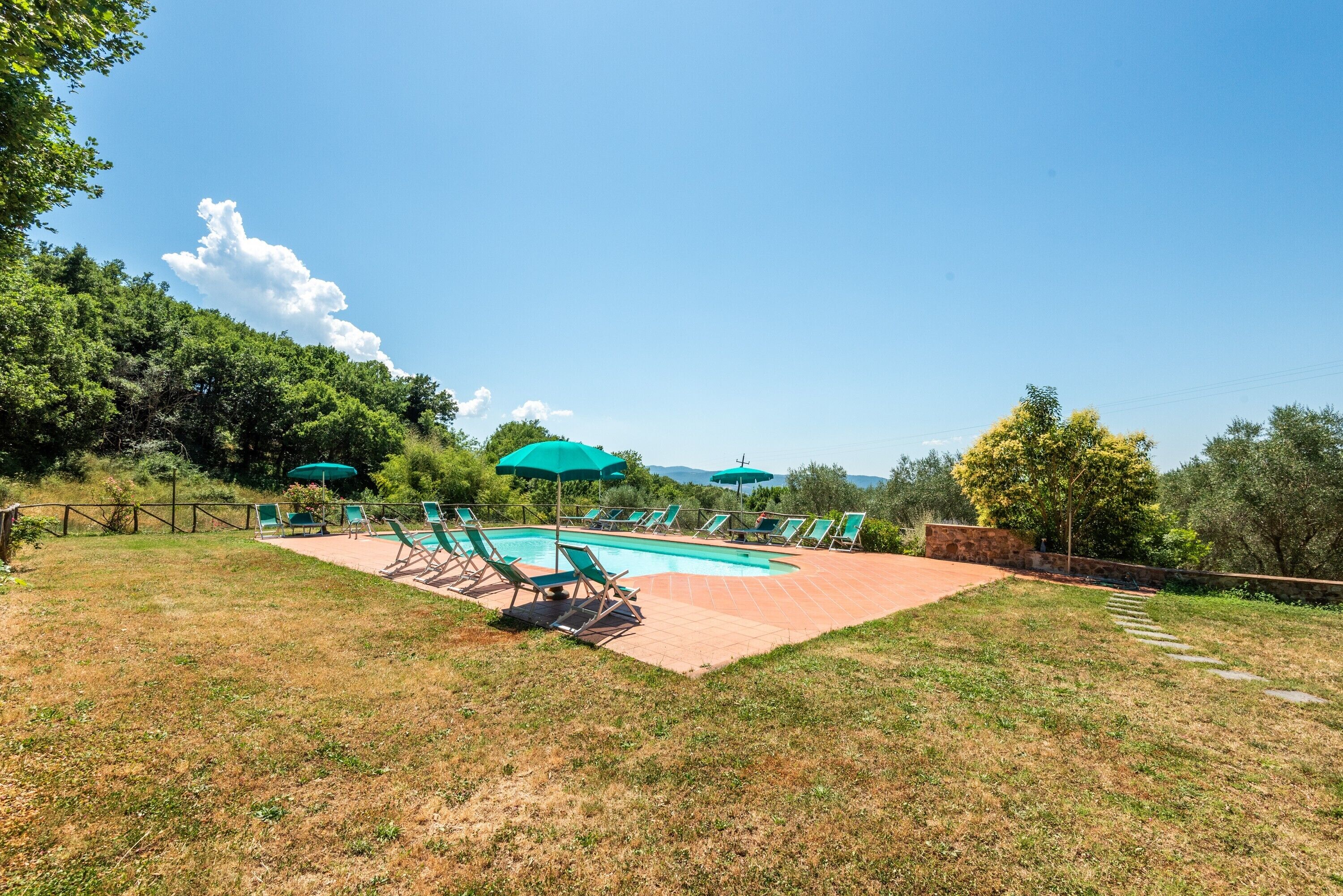 Une piscine entourée d’une pelouse et d’arbres, avec des chaises longues et des parasols à proximité.