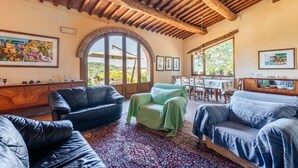A spacious living room with a high wooden ceiling, a large arched window, and a dining area with a table and chairs.
