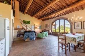 Un interior rústic amb sostre de fusta, zona de menjador amb taula i cadires, i una finestra gran d'arc.