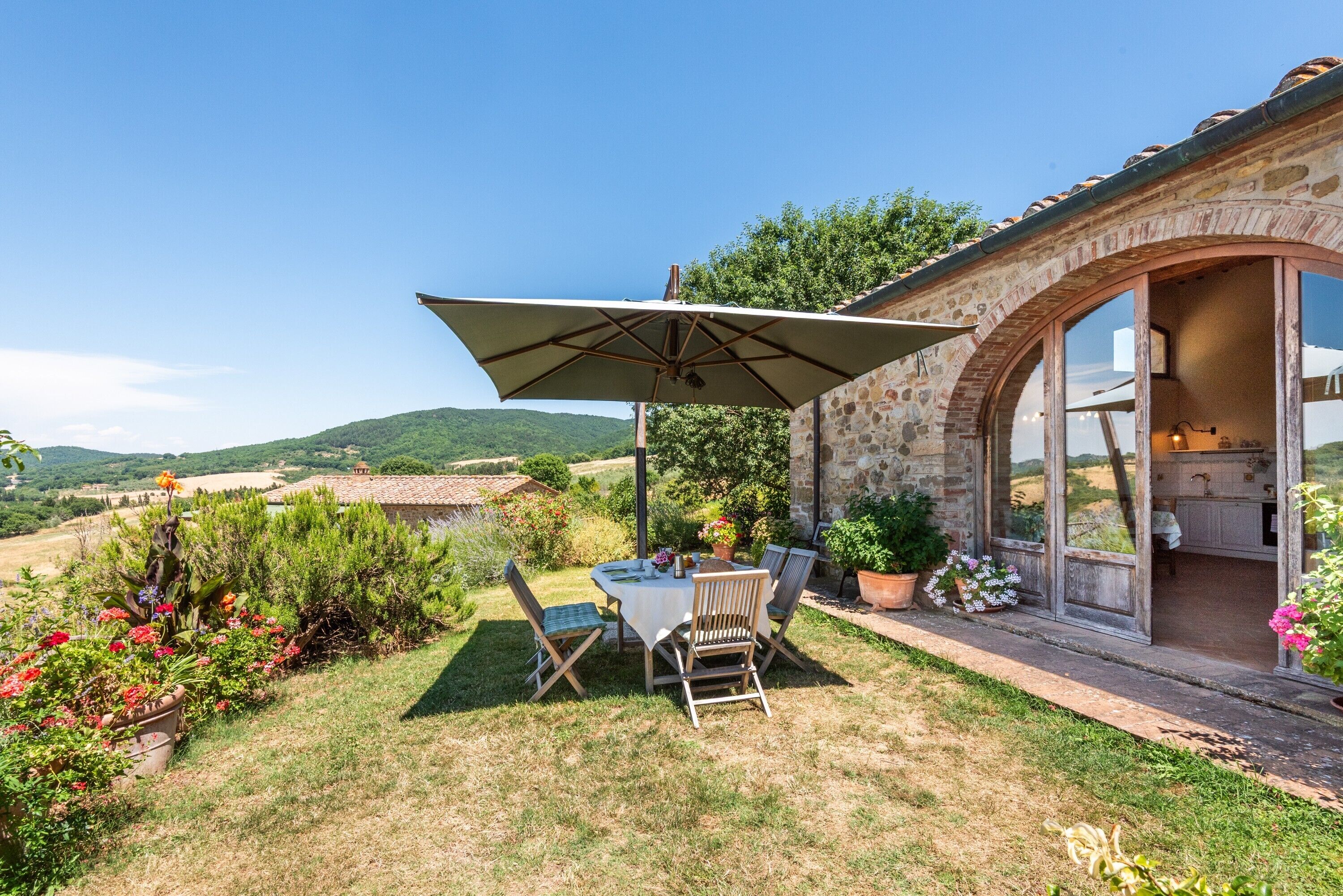 A patio with a table and chairs, a large umbrella, and a stone building with an open door.