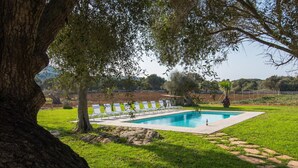 Una piscina con sillas de descanso, rodeada de césped y árboles.