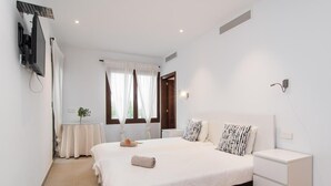 Un dormitorio con cama, mesitas de noche, televisor y ventana con cortinas.