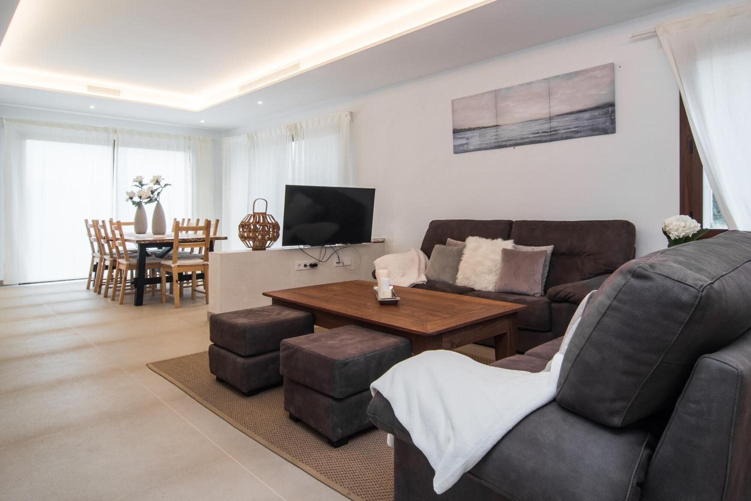 Ein modernes Wohnzimmer mit einer Couch, Hocker, einem Couchtisch, einem Fernseher und einem Essbereich mit Stühlen und einem Tisch.
