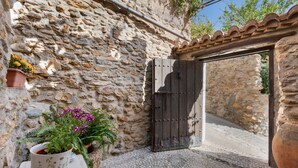 Un muro de piedra con una puerta de madera, una planta en maceta y un suelo de baldosas.