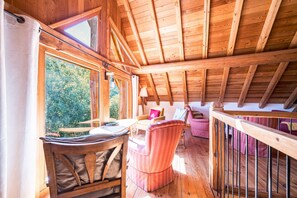 A wooden interior with a high ceiling, a dining area with a table and chairs, and a view of greenery outside. - Chalet 'La Grange Des Flocons' with Mountain View, Private Terrace and Private Garden (Valloire)