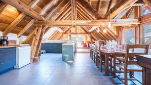 An attic-style room with exposed wooden beams, a kitchen area with modern appliances, and a dining table set for four. - Chalet 'La Grange Des Flocons' with Mountain View, Private Terrace and Private Garden (Valloire)
