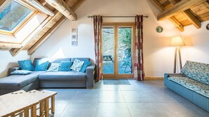 A loft-style room with a wooden ceiling, a sofa, a table, and a view through a glass door. - Chalet 'La Grange Des Flocons' with Mountain View, Private Terrace and Private Garden (Valloire)