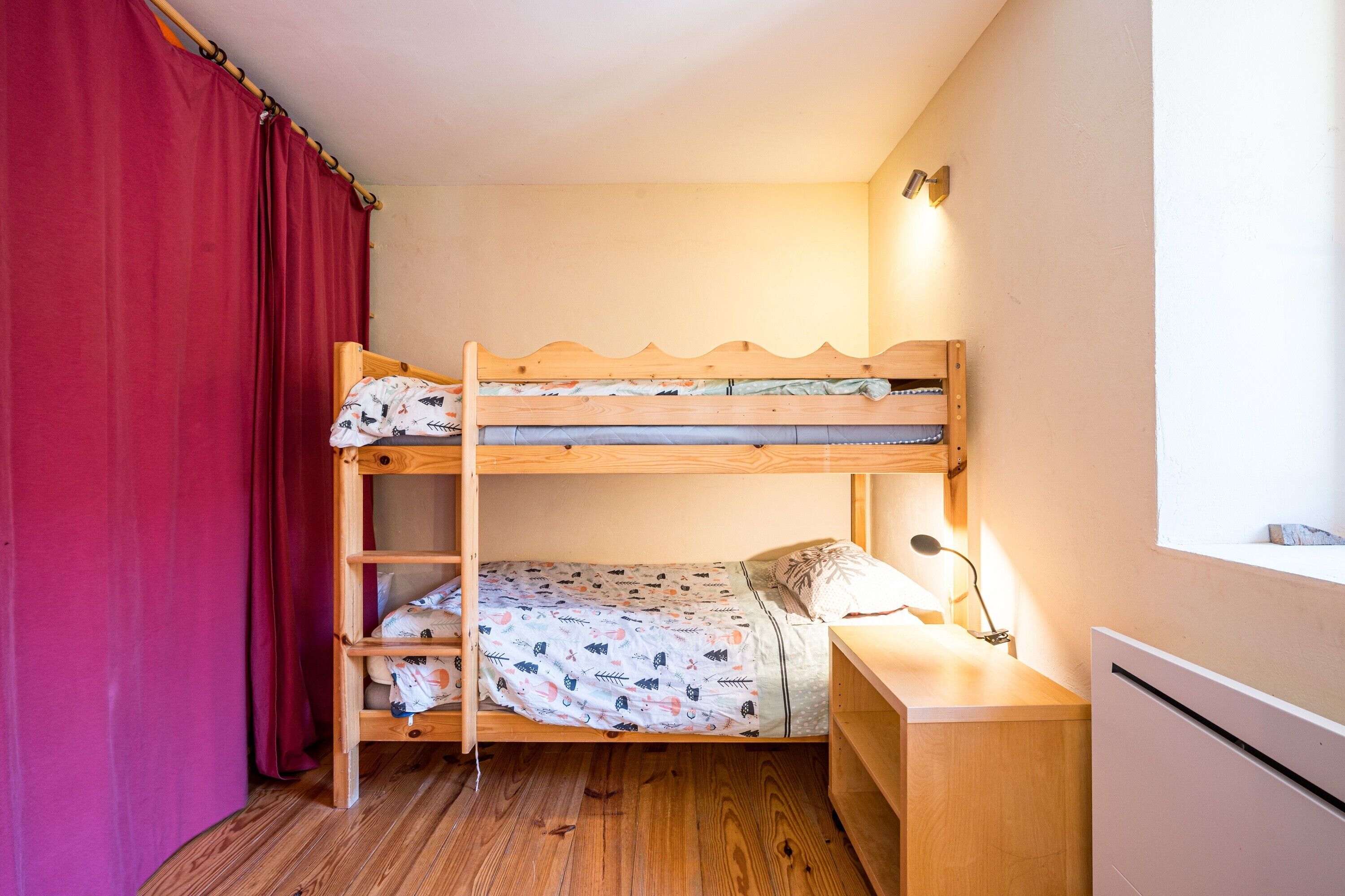 Een stapelbed met houten frame, een bureau met lamp en een raam.