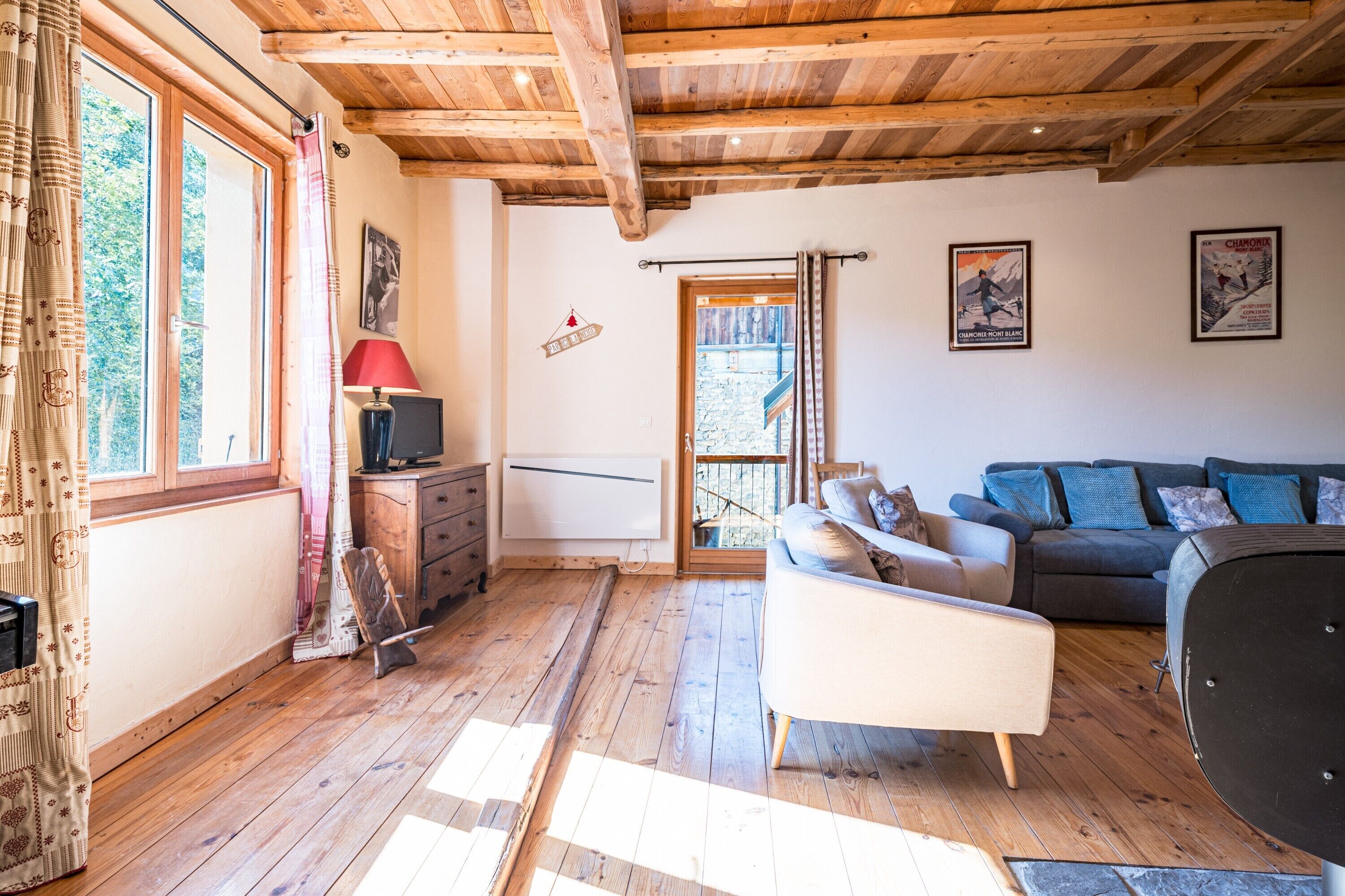Habitación con suelo de madera, un sofá, un televisor y una ventana con cortinas.