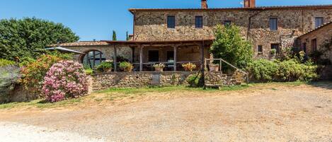 A stone building with a porch, a well-maintained garden, and a gravel driveway.