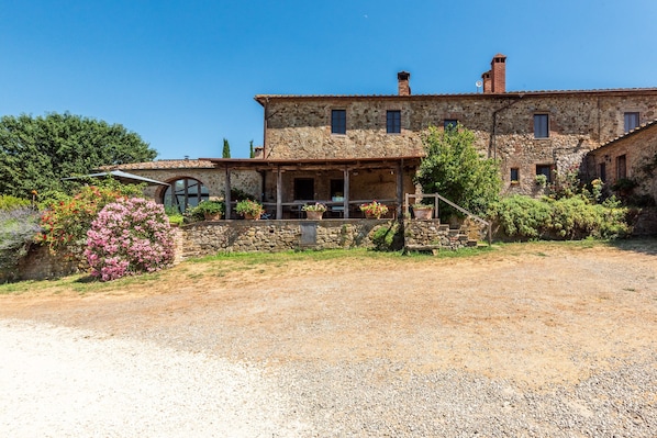 A stone building with a porch, a well-maintained garden, and a gravel driveway.